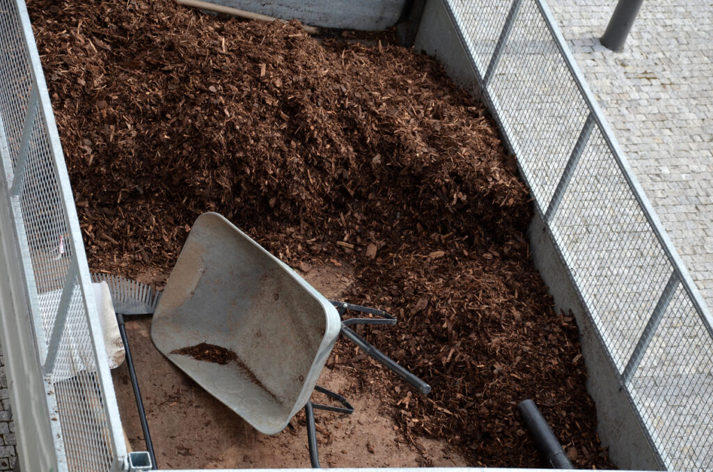 loading torture wood chips bark on a wheelbarrow with a shovel from a car and delivery to the garden where ornamental perennial beds are mulched by gardeners, upper view, metal grate