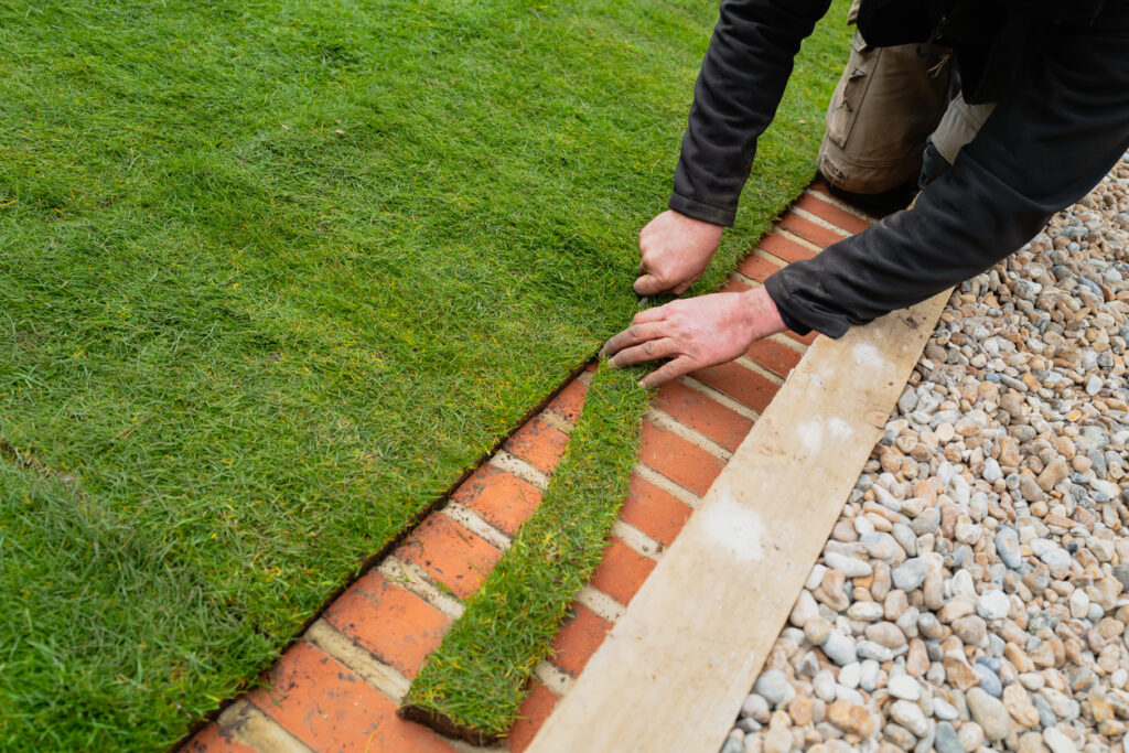 A man trimming newly laid natural turf along the brick mowing strip at the edge of the lawn